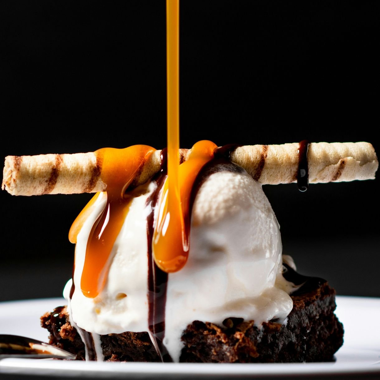 Chocolate brownie with orange sauce poured from above topped with ice cream