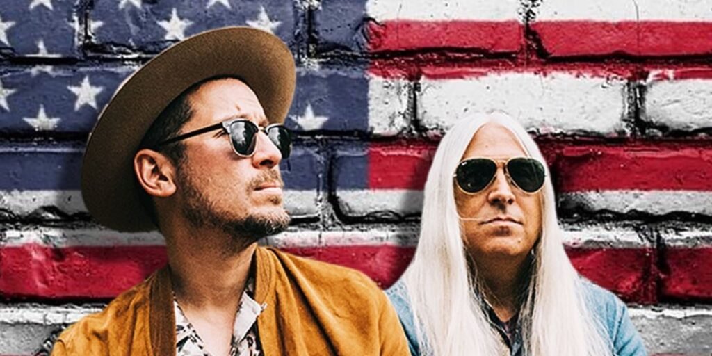 Man on left wearing cowboy hat and brown jacket standing next to man with long white hair with US flag in background